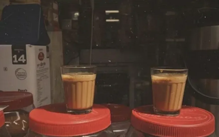 Two cutting chai glasses resting on biscuit jars at a street stall